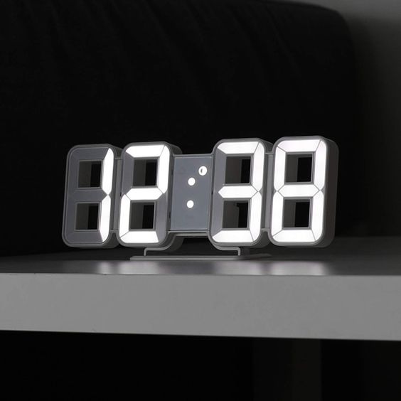 VibeCore 3D LED Digital Alarm Clock in white with white light, angled front view. Featuring bold, illuminated 3D LED digits for easy readability, this modern alarm clock also includes a thermometer, perpetual calendar, and moon phase display. Its sleek rectangular design adds a contemporary touch to any room, enhancing your space with both style and function.
