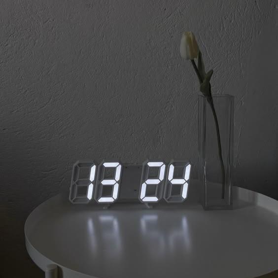 VibeCore 3D LED Digital Alarm Clock in white with white light, displayed on side table. Featuring bold, illuminated 3D LED digits for easy readability, this modern alarm clock includes a thermometer, perpetual calendar, and moon phase display. Its sleek, rectangular design adds a stylish, contemporary touch to any space, making it a perfect addition to your bedside or living room.