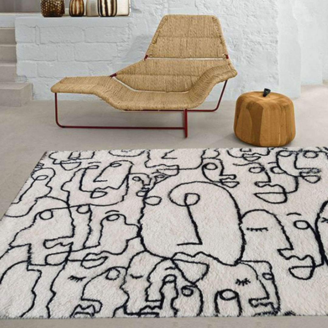 VibeCore Abstract Faces Rug in a living room, close-up view showing intricate black and white abstract face designs, with plush texture on a hardwood floor.