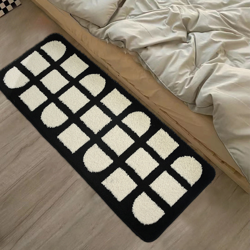 VibeCore Aesthetic Abstract Rug positioned at the foot of a bed, showcasing its minimalist black and white geometric design. The soft, plush texture and non-slip backing are visible, adding a modern, stylish touch to the bedroom space.