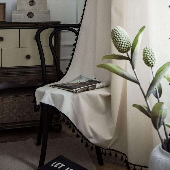 Beige tassel linen curtain draped on a chair, showcasing soft fabric and tassel accents.