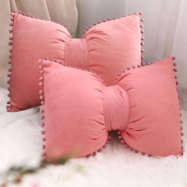 VibeCore Classic Bow Throw Pillow in coral pink, two pillows stacked together, featuring a playful bow shape with pom-pom details, adding a chic and fun touch to room decor.