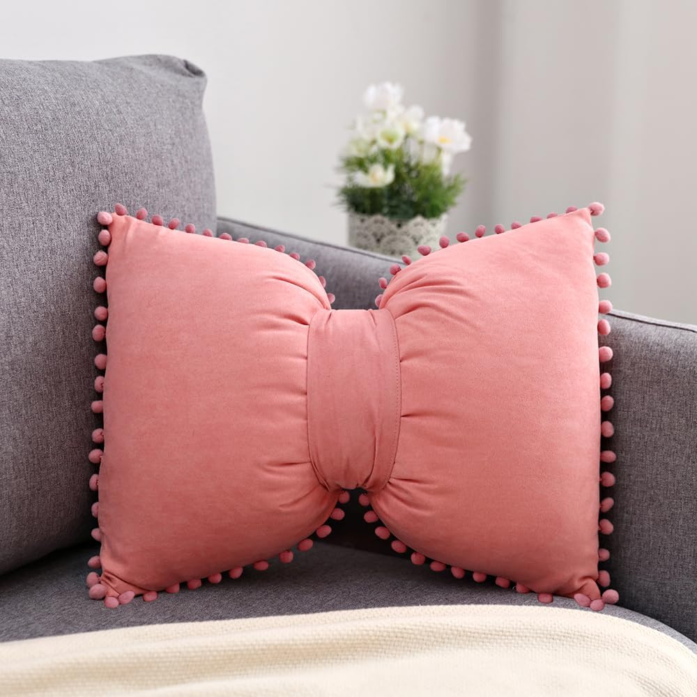VibeCore Classic Bow Throw Pillow in coral pink, featuring a cute bow shape with pom-pom details, adding a playful and chic touch to any room decor.