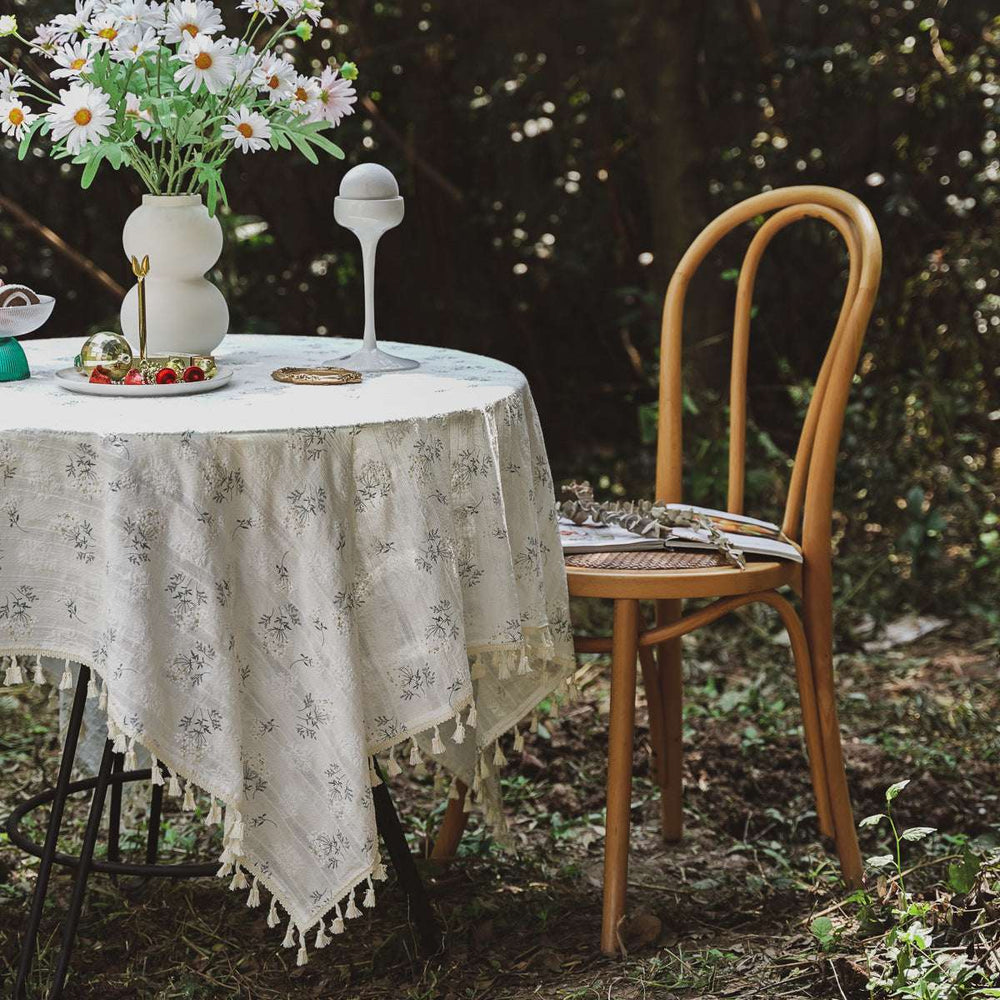 VibeCore Clove Flower Tassel Linen Tablecloth with floral patterns and tassel edges, elegantly laid on a table outside, enhancing the outdoor dining experience with a touch of elegance and style.