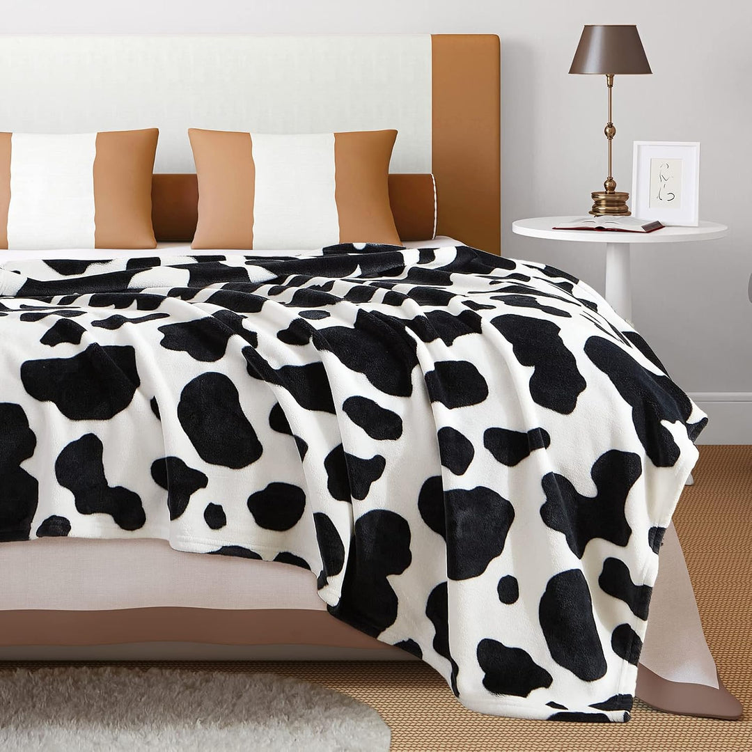 Close-up of a black cow print throw blanket on a bed, highlighting its bold design and soft texture. A cozy and stylish accent for your bedroom.