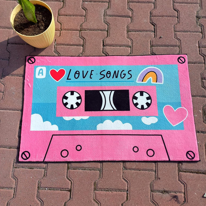 VibeCore Cute Cassette Accent Rug in pink, laid flat on the ground, featuring a vibrant retro cassette tape design. Its soft, plush texture adds comfort and style to the space, with a non-slip backing ensuring safety.