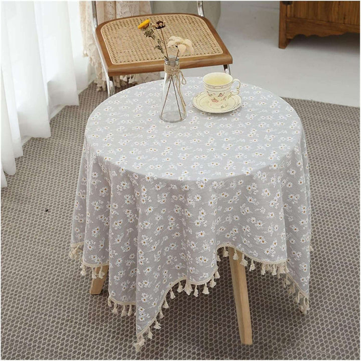 VibeCore Daisy Embroidered Linen Tablecloth in gray, placed on a round table, featuring delicate daisy embroidery and tassel accents for an elegant and fresh dining setting.