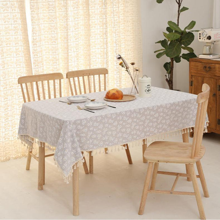 VibeCore Daisy Embroidered Linen Tablecloth in gray, laid on a square table, showcasing delicate daisy embroidery and tassel details for a stylish and charming table setting.