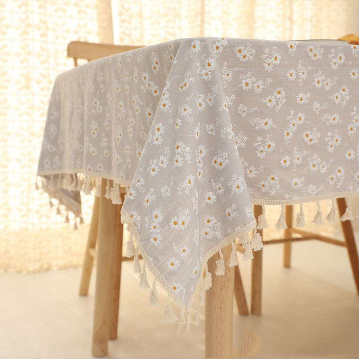 VibeCore Daisy Embroidered Linen Tablecloth in gray, close-up of the corner on a square table, featuring delicate daisy embroidery and tassel accents for a charming and elegant look.