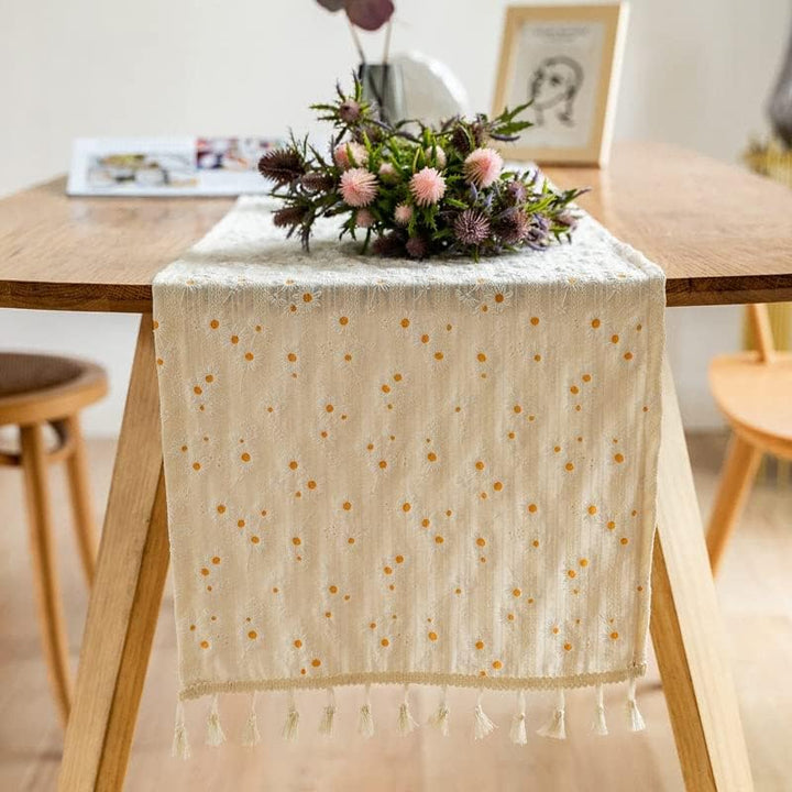 VibeCore Daisy Embroidered Linen Tablecloth in white, folded neatly on a table, showcasing delicate daisy embroidery and tassel accents for a fresh and elegant dining decor.