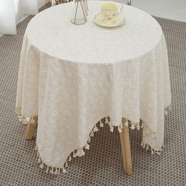 VibeCore Daisy Embroidered Linen Tablecloth in white, elegantly placed on a round table, featuring delicate daisy embroidery and tassel accents for a fresh, charming dining ambiance.