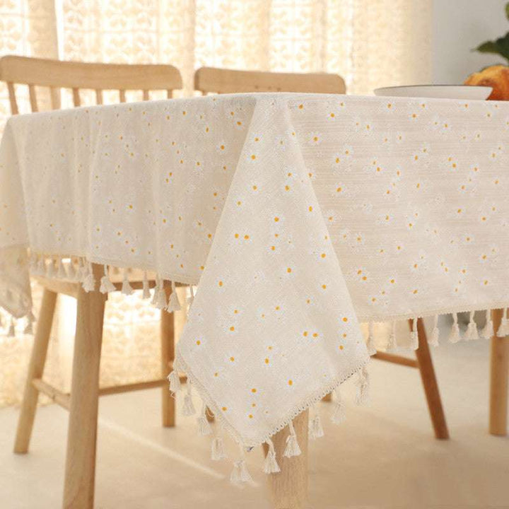 VibeCore Daisy Embroidered Linen Tablecloth in white, close-up of the corner on a square table, highlighting the delicate daisy embroidery and tassel accents for a fresh and elegant touch.