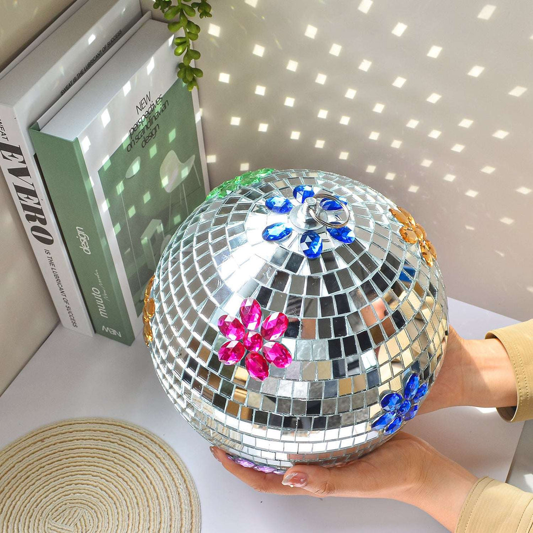 Floral Hanging Disco Ball, an elegant and playful decor piece featuring embroidered glass with floral patterns on a silver inlay. The reflective surface creates a dazzling effect, perfect for any space or celebration.