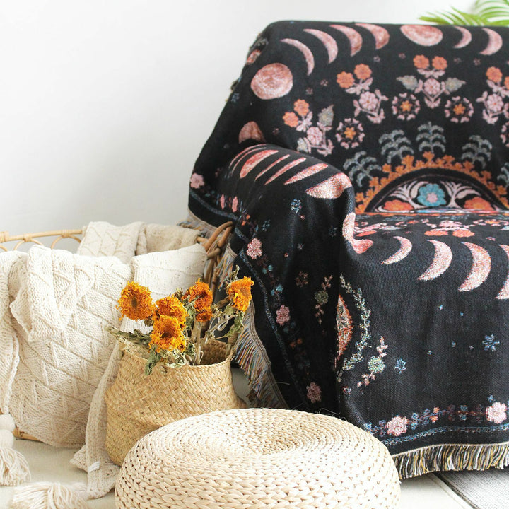 Floral Phases of the Moon Woven Blanket draped over a chair close-up, highlighting its celestial and floral patterns. Made from 100% combed cotton, this versatile piece adds a mystical, cozy vibe to your space.
