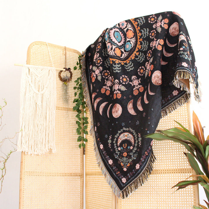 Floral Phases of the Moon Woven Blanket draped over a divider, showcasing its celestial and floral patterns. Made from 100% combed cotton, this versatile piece adds a mystical, serene touch to any space.