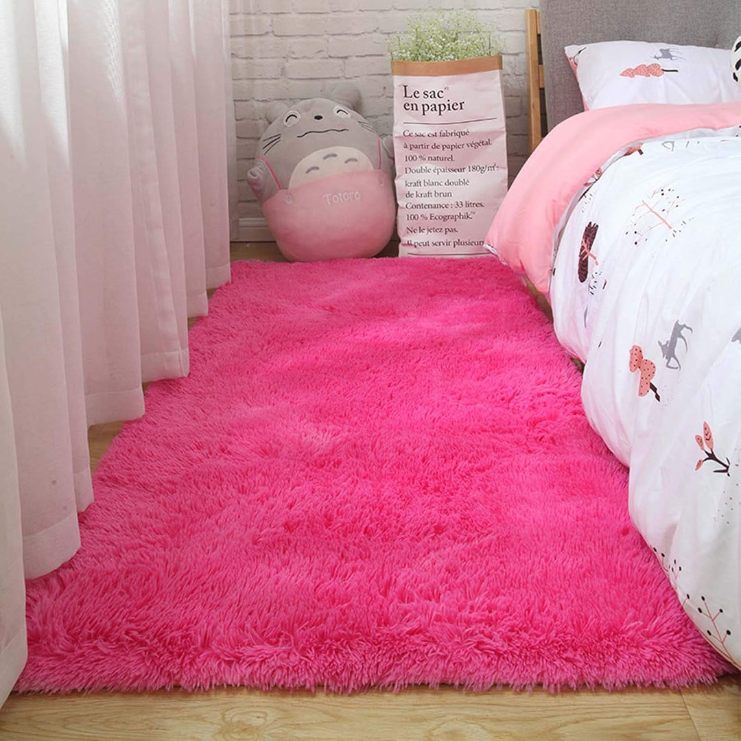 VibeCore Fluffy Area Rug in Rose Red placed beside a bed, adding a warm, plush touch to the room's decor with its soft texture and bold color.