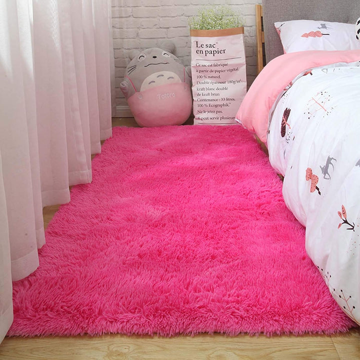 VibeCore Fluffy Area Rug in Rose Red placed beside a bed, adding a warm, plush touch to the room's decor with its soft texture and bold color.