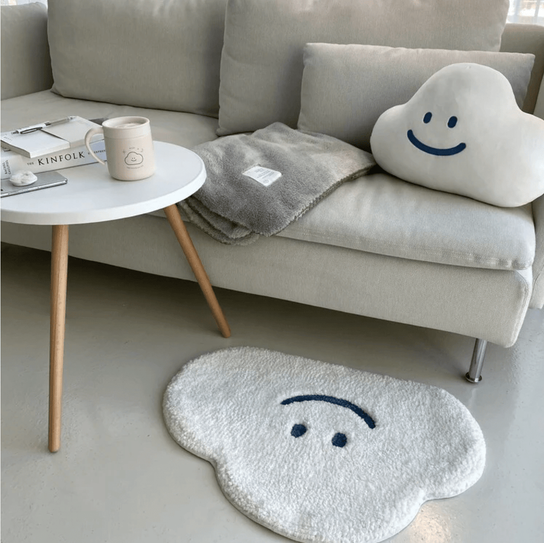 Aesthetic aerial view of the "Happy Cloud Accent Rug" beside a couch, featuring its playful cloud design with a cheerful face. This soft, round rug adds a cozy, positive vibe to the space, with a plush texture and non-slip backing ensuring comfort and safety in any room.