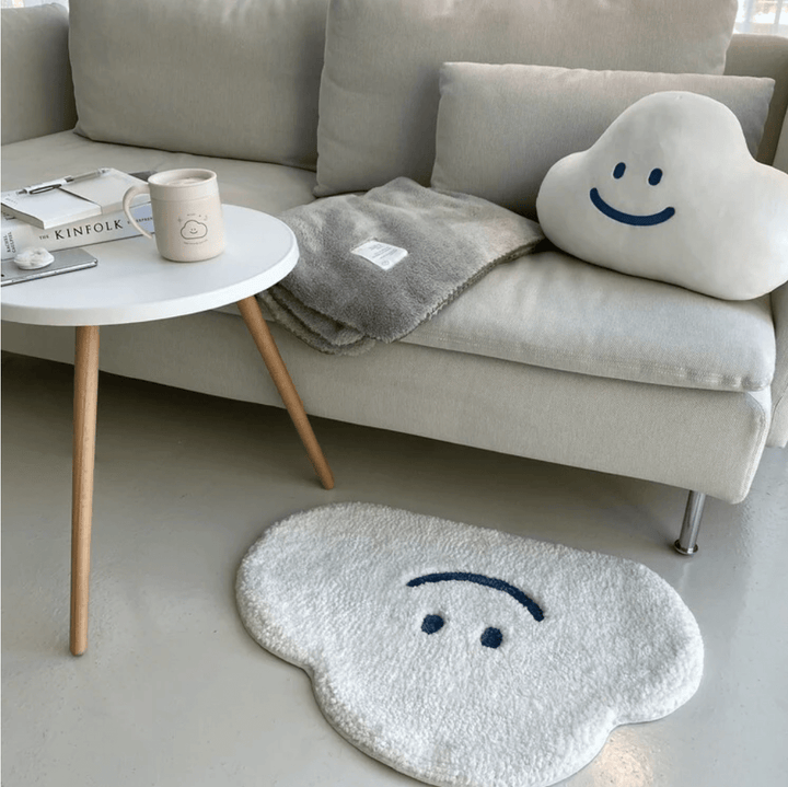 Aesthetic aerial view of the "Happy Cloud Accent Rug" beside a couch, featuring its playful cloud design with a cheerful face. This soft, round rug adds a cozy, positive vibe to the space, with a plush texture and non-slip backing ensuring comfort and safety in any room.