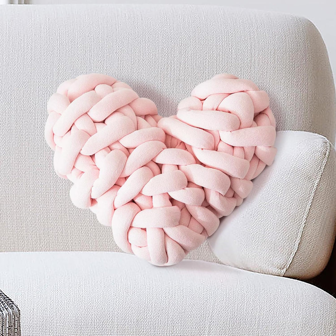 VibeCore Heart-Shaped Knot Throw Pillow in baby pink, placed on a couch, featuring its heart-shaped, woven knot design. This plush, cozy pillow adds a charming and loving touch to your living space, creating a warm, inviting atmosphere.