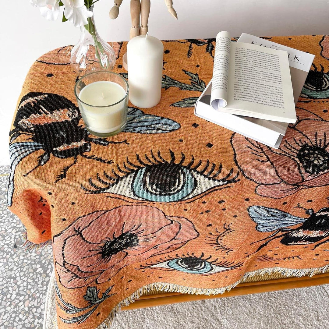 VibeCore Honey Dreams Woven Blanket as tablecloth, showcasing a detailed bee motif and captivating eye patterns. Made from soft, breathable 100% combed cotton, it adds warmth, charm, and a unique vibe to your table while elevating your space with its reversible design.