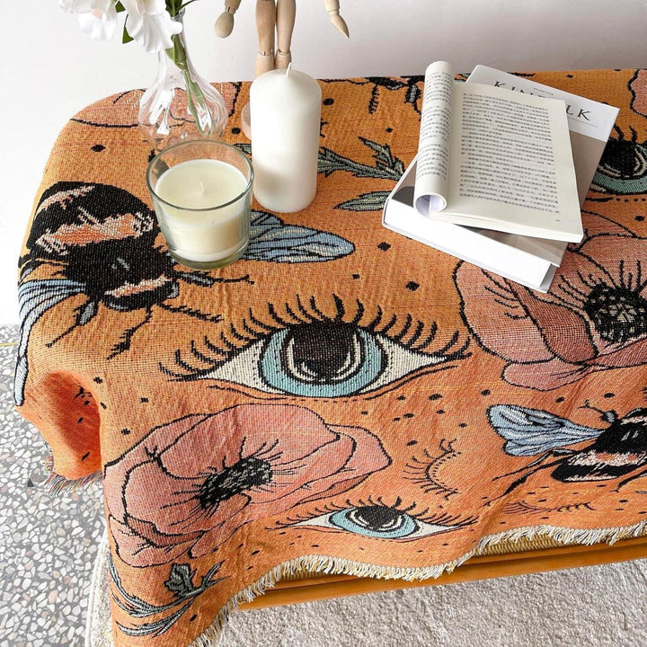 VibeCore Honey Dreams Woven Blanket as tablecloth, showcasing a detailed bee motif and captivating eye patterns. Made from soft, breathable 100% combed cotton, it adds warmth, charm, and a unique vibe to your table while elevating your space with its reversible design.