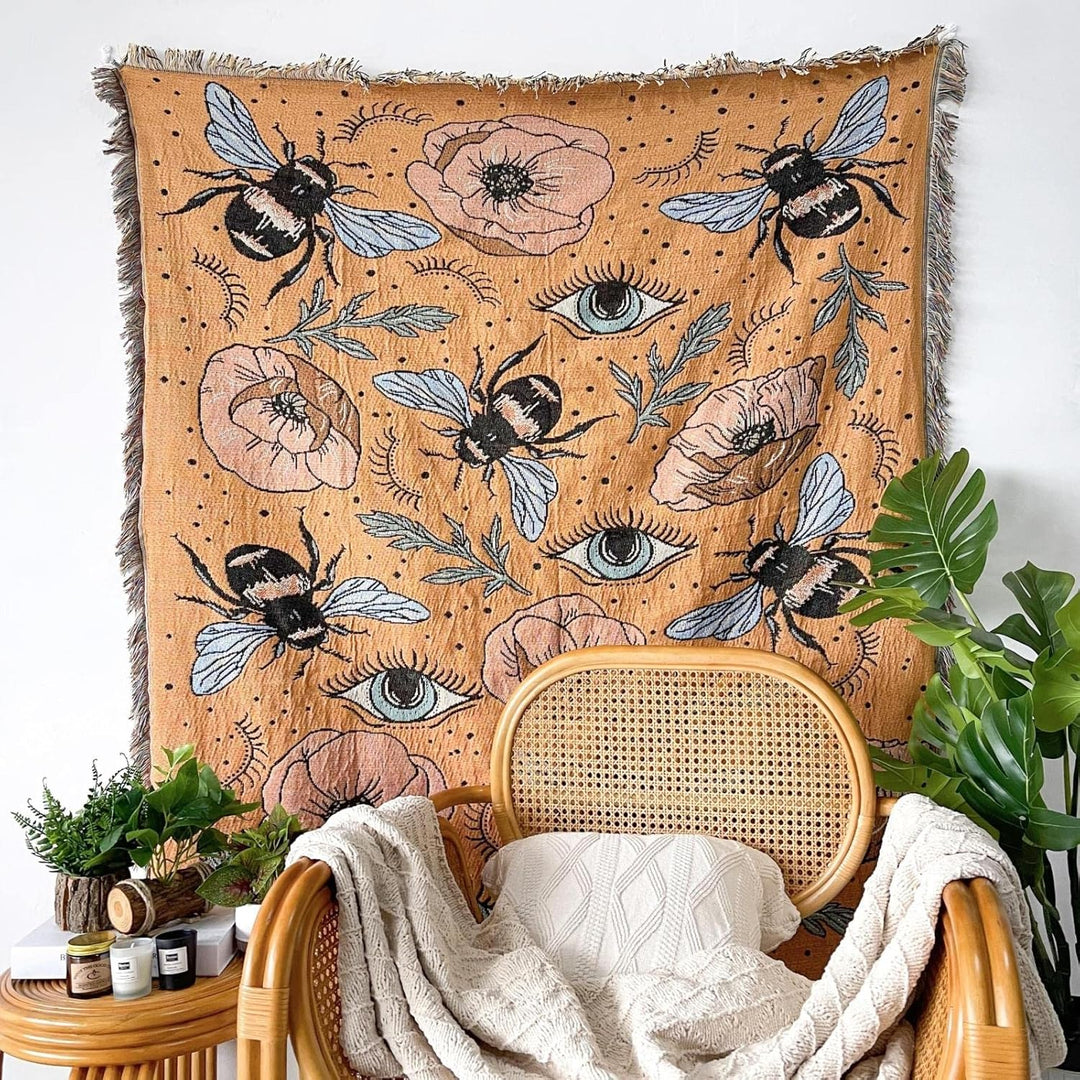 VibeCore Honey Dreams Woven Blanket as wall hanging, featuring a detailed bee motif and captivating eye patterns. Made from soft, breathable 100% combed cotton, it adds a warm, charming touch and unique style to your space, turning any wall into an eye-catching focal point.