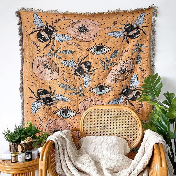 VibeCore Honey Dreams Woven Blanket as wall hanging, featuring a detailed bee motif and captivating eye patterns. Made from soft, breathable 100% combed cotton, it adds a warm, charming touch and unique style to your space, turning any wall into an eye-catching focal point.
