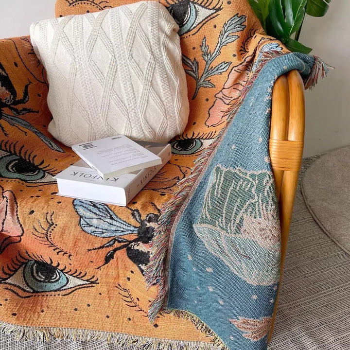 VibeCore Honey Dreams Woven Blanket close-up on chair, highlighting the detailed bee motif and captivating eye patterns. Crafted from soft, breathable 100% combed cotton, it adds warmth, charm, and a unique touch, elevating the style of your space.