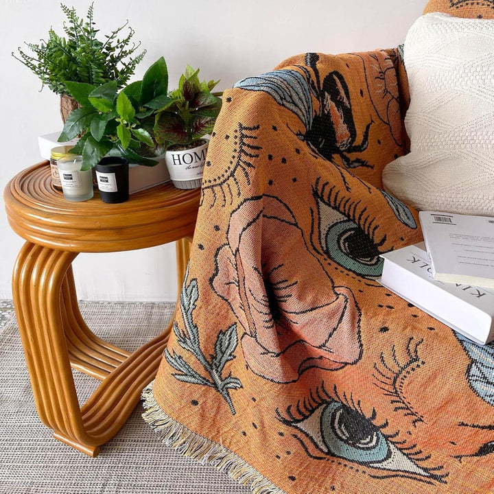 VibeCore Honey Dreams Woven Blanket close-up on couch, showcasing the detailed bee motif and captivating eye patterns. Made from soft, breathable 100% combed cotton, it adds warmth, charm, and a unique vibe, elevating the comfort and style of your space.