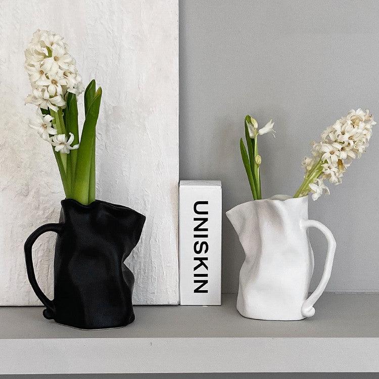 VibeCore Irregularly Folded Ceramic Vase in White and Black with Flowers in It, showcasing a sculptural, minimalist design on a modern table.