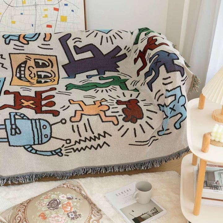 VibeCore Keith Haring Graffiti Woven Blanket completely covering couch, close-up view showcasing vibrant street art design and detailed 100% cotton texture.