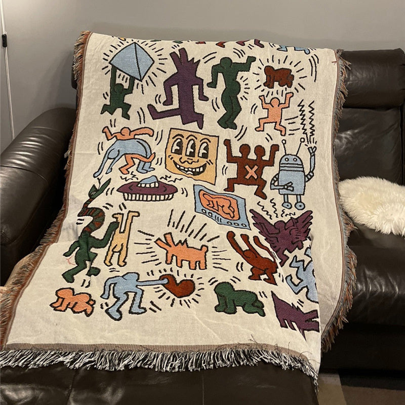 VibeCore Keith Haring Graffiti Woven Blanket completely splayed out on the corner of couch, close-up highlighting vibrant street art design and soft 100% cotton texture.