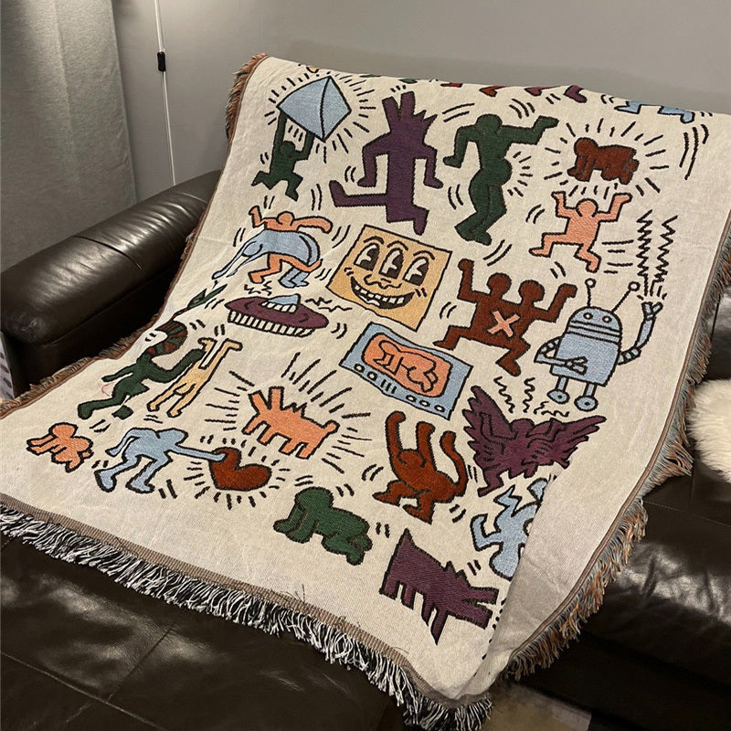 VibeCore Keith Haring Graffiti Woven Blanket laid out on couch, featuring bold street art design in vibrant 100% cotton fabric.