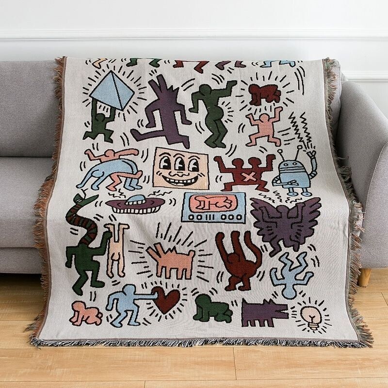 VibeCore Keith Haring Graffiti Woven Blanket on couch, showcasing vibrant street art pattern and soft 100% cotton texture.