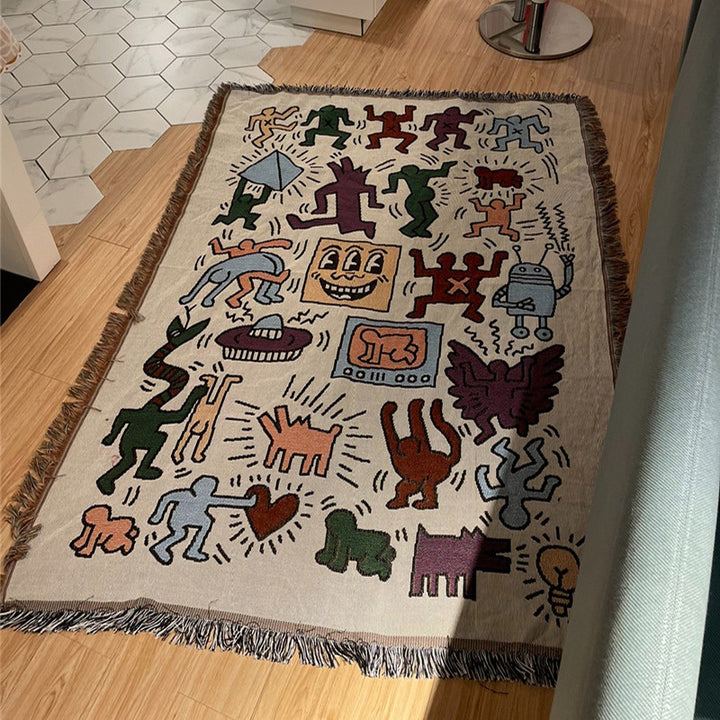 VibeCore Keith Haring Graffiti Woven Blanket on floor, displaying vibrant street art design and soft 100% cotton texture.