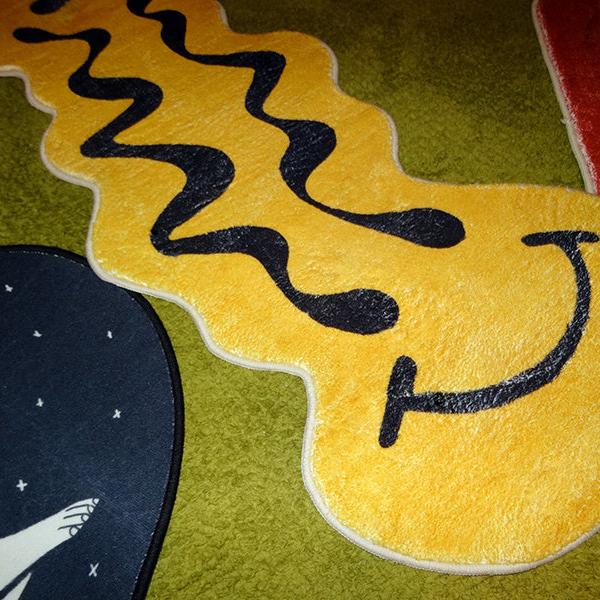 VibeCore Melted Smiley Accent Rug on carpet, angled close-up view highlighting the bold, dripping smiley face design and plush texture.