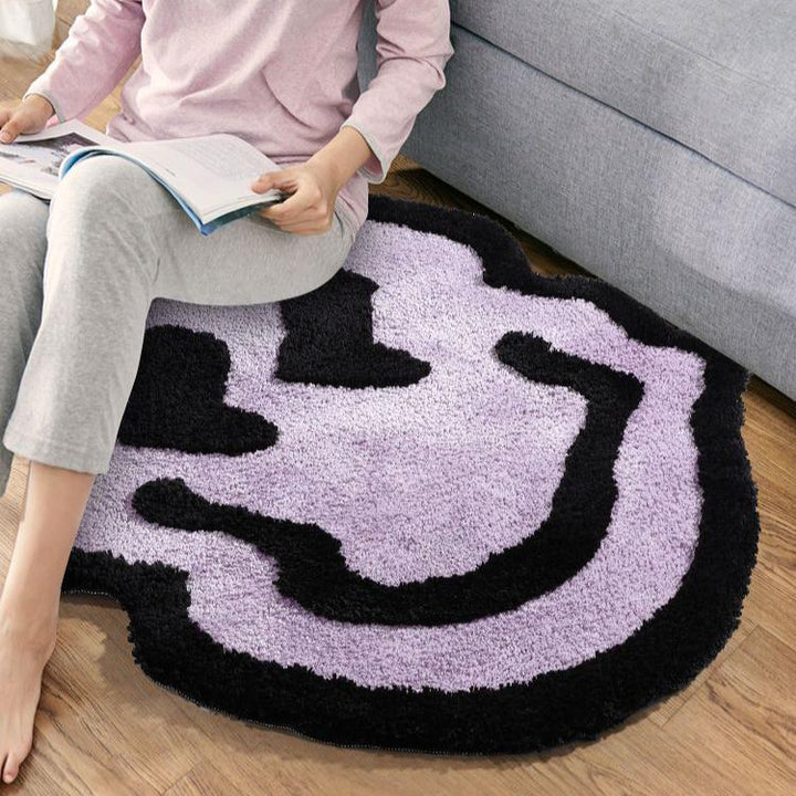 VibeCore Melting Smiley Accent Rug Purple Woman Sitting On It, highlighting the cheerful, bold design and plush comfort of the rug, creating a playful and cozy atmosphere in the room.