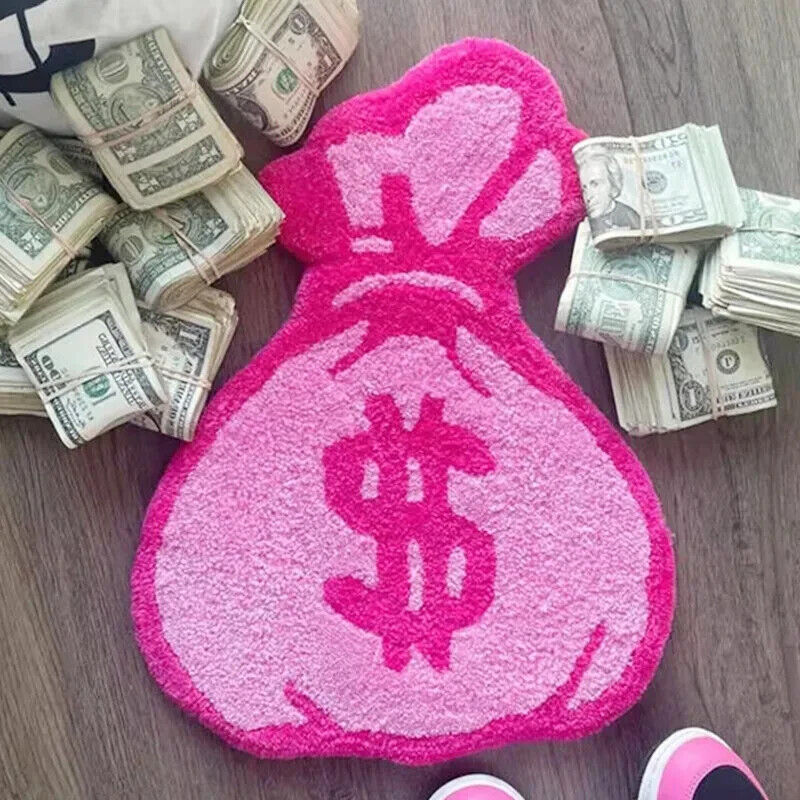 Top-down view of the VibeCore Pink Cartoon Money Bag Accent Rug surrounded by scattered money, highlighting its playful pink money bag design. This vibrant rug brings a fun and quirky touch to any room, perfect for those seeking girly, urban, or contemporary decor. Its soft texture and non-slip backing make it both stylish and safe. Ideal for bedrooms, dorm rooms, or living areas, this cute rug adds personality and a pop of color to your space.