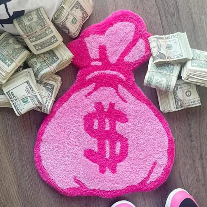 Top-down view of the VibeCore Pink Cartoon Money Bag Accent Rug surrounded by scattered money, highlighting its playful pink money bag design. This vibrant rug brings a fun and quirky touch to any room, perfect for those seeking girly, urban, or contemporary decor. Its soft texture and non-slip backing make it both stylish and safe. Ideal for bedrooms, dorm rooms, or living areas, this cute rug adds personality and a pop of color to your space.