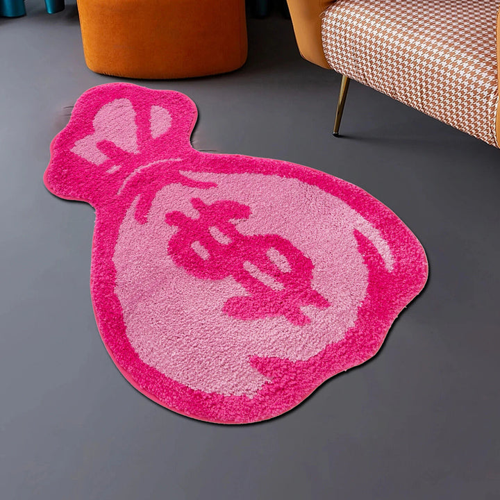 Angled aerial view of the VibeCore Pink Cartoon Money Bag Accent Rug, showcasing its vibrant pink color and playful money bag design. Perfect for adding a fun, girly touch to any space, this rug brings personality and charm to bedrooms, dorms, or living rooms. The soft, plush texture and non-slip backing make it both comfortable and safe, while the bold design adds a unique flair to your decor.