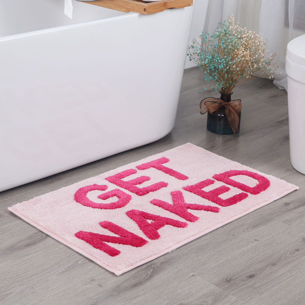 Aesthetic "Pink Get Naked Bath Mat" displayed in front of a tub, featuring a vibrant pink color and playful design. The soft, plush texture adds comfort to your bathroom while the non-slip backing ensures stability and safety, making it the perfect fun addition to your space.