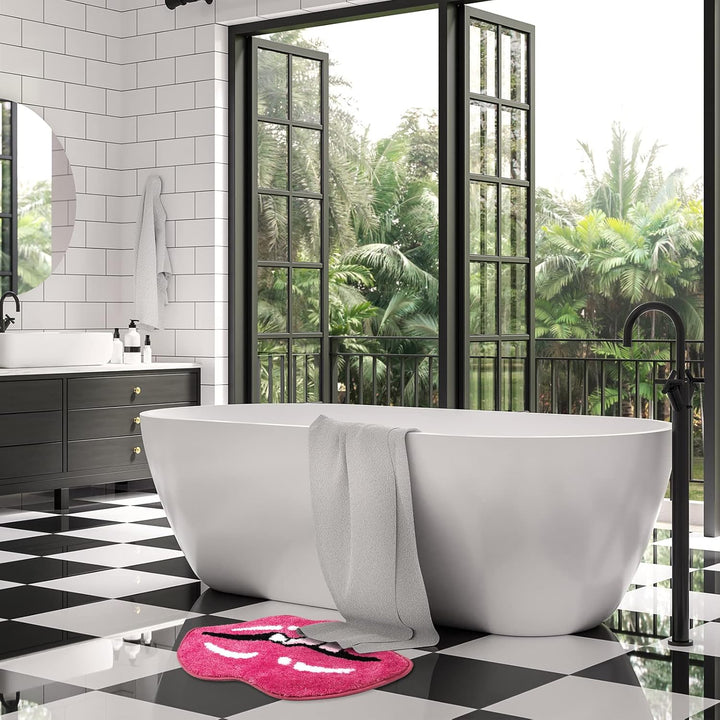 The VibeCore Pink Lips Tongue Out Accent Rug placed in front of a tub, featuring a bold pink lip and tongue design. This playful accent rug adds a fun and cozy touch to the bathroom while providing a soft feel and anti-slip backing for safety.