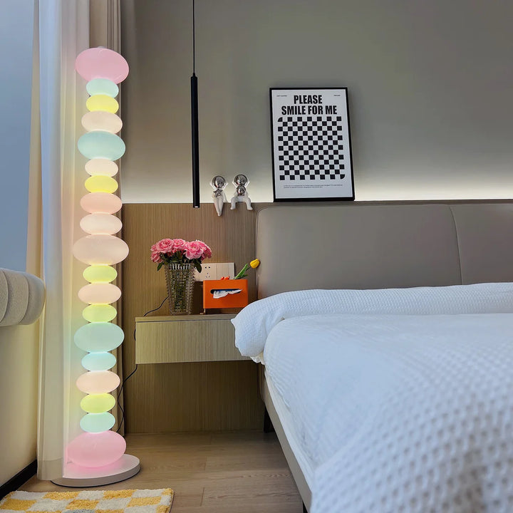 The Rainbow Candy Floor Lamp illuminating a cozy bedroom, casting a soft, colorful light that adds a playful yet calming ambiance, perfect for enhancing the room's eclectic, welcoming vibe.