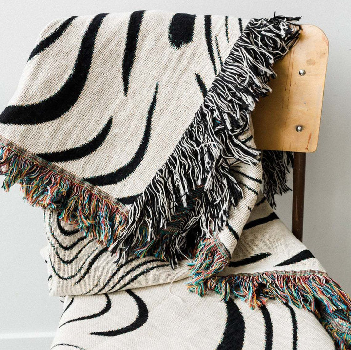 VibeCore Retro Marble Wave Woven Blanket folded over chair, featuring spiritual-inspired cosmic design and soft 100% combed cotton texture.