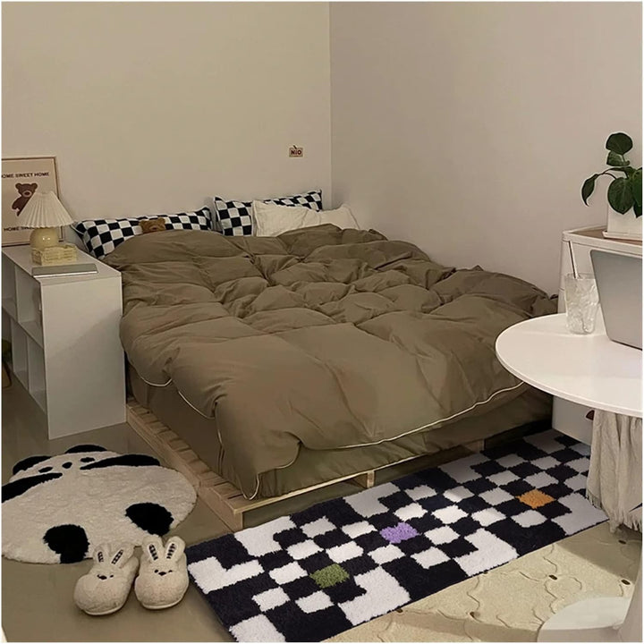 The VibeCore Retro Remix Accent Rug with a bold checkered design placed at the foot of a bed, adding a stylish and colorful retro vibe to the room. The plush texture enhances the cozy atmosphere.