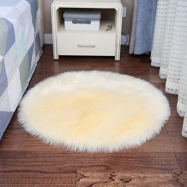 VibeCore Round Faux Fur Accent Rug in beige placed beside a bed. Soft and fluffy with a non-slip backing, ideal for adding comfort to bedrooms or dorm rooms. Easy to clean, available in multiple colors.