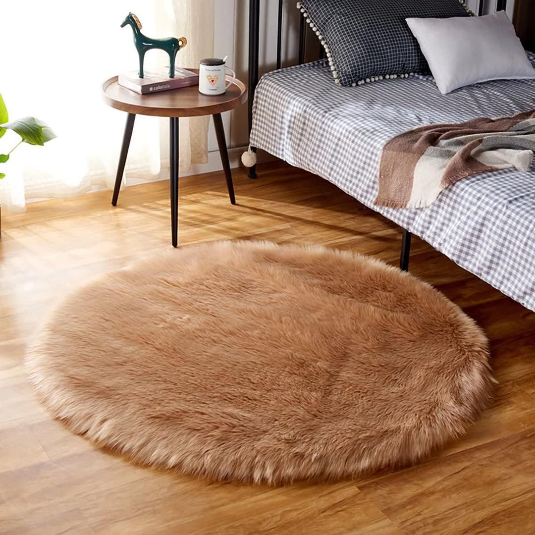 VibeCore Round Faux Fur Accent Rug in khaki placed beside a bed. Soft and fluffy with a non-slip backing, ideal for adding comfort to bedrooms or dorm rooms. Easy to clean, available in multiple colors.