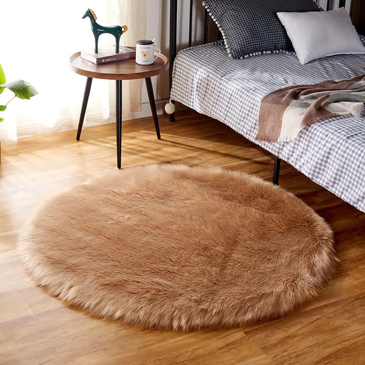 VibeCore Round Faux Fur Accent Rug in khaki placed beside a bed. Soft and fluffy with a non-slip backing, ideal for adding comfort to bedrooms or dorm rooms. Easy to clean, available in multiple colors.