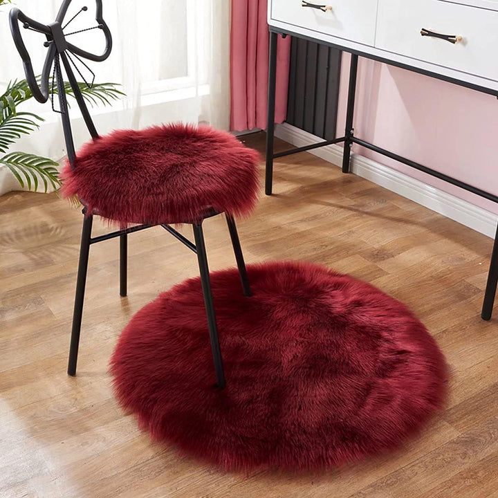 VibeCore Round Faux Fur Accent Rug in red on the floor, also used as a seat cover. Soft, fluffy texture with a non-slip backing, perfect for bedrooms, living rooms, or dorm rooms. Easy to clean, available in multiple colors.